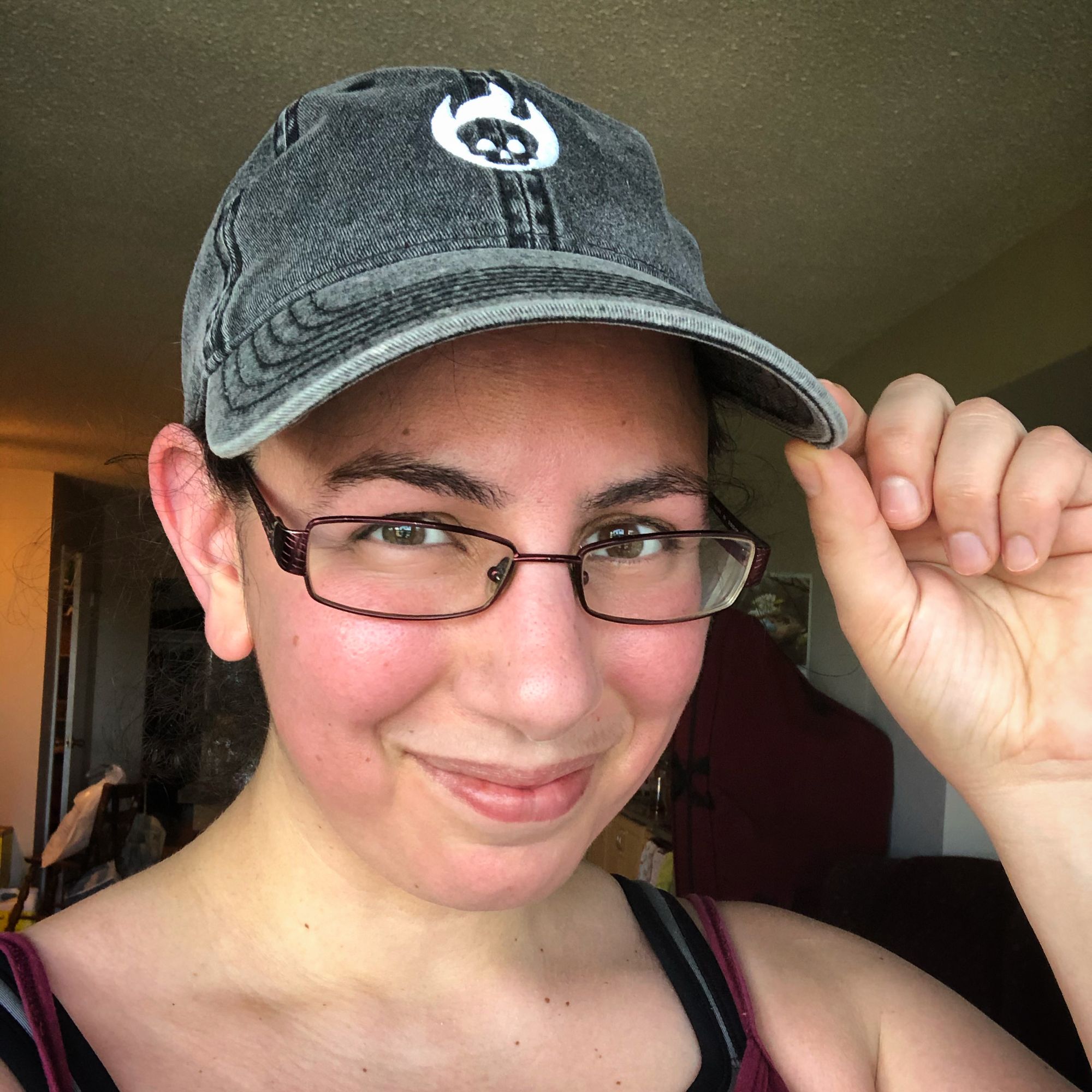 Selfie: close up on my sweaty pink post-run face while wearing a grey denim blaseball cap, featuring a stylized logo of a white embroidered skull engulfed in flame. I'm touching the brim of the cat with two fingers in a kind of salute to show off the merch.