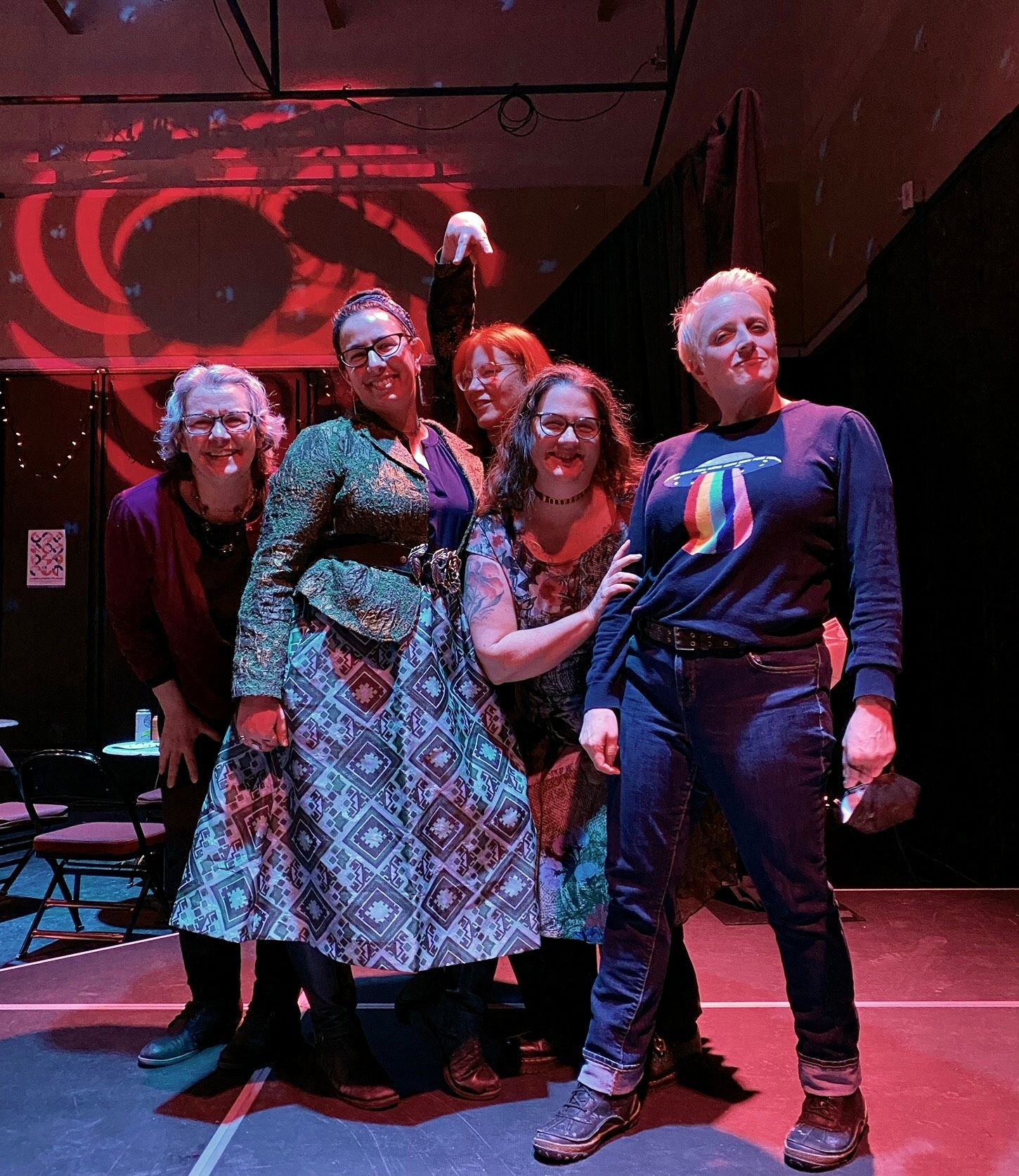 The five of us are striking a pose together on a stage while extravagant red and blue lighting swirls around us.