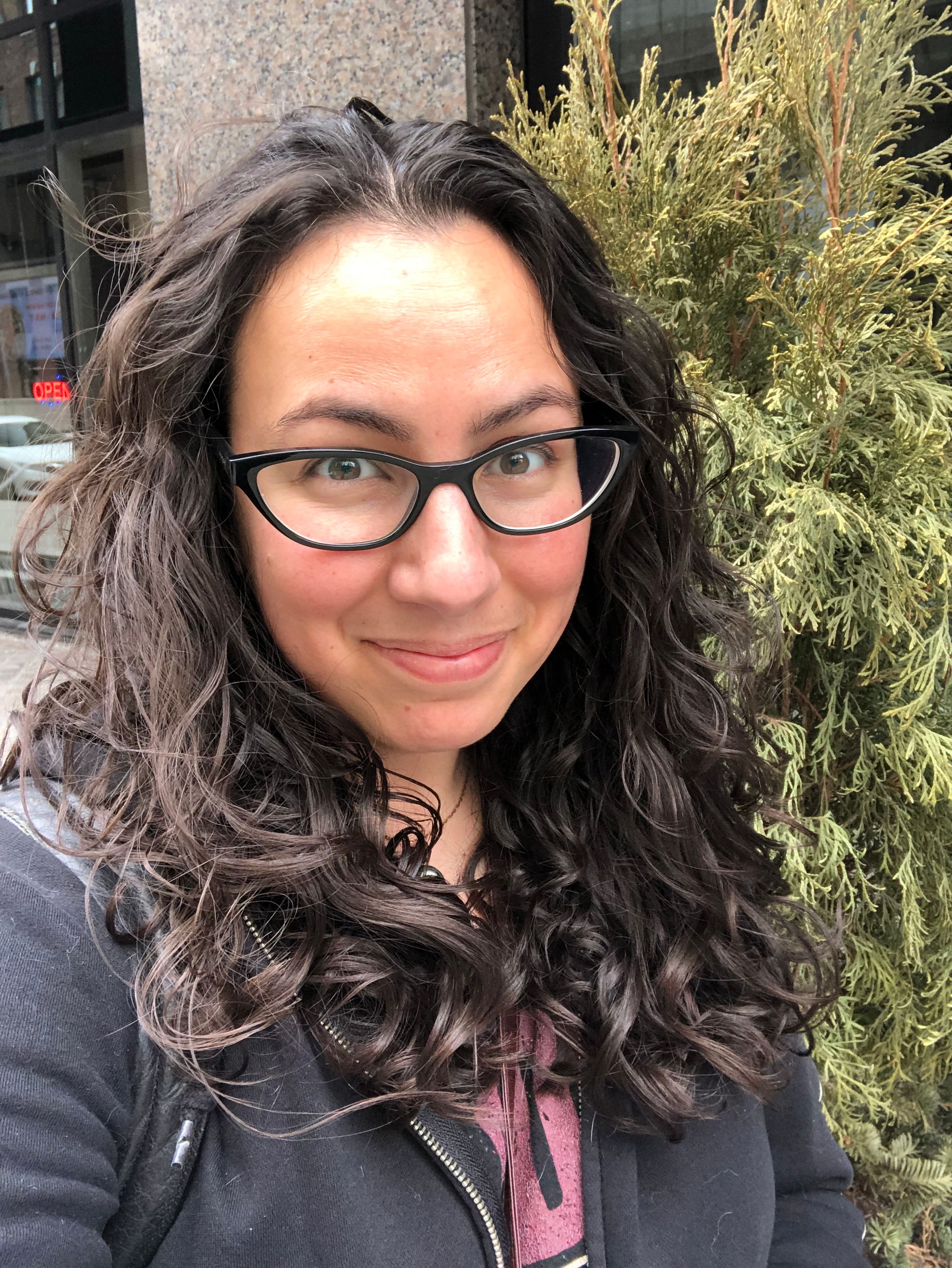 Outdoor selfie of me looking super delighted with my hair in very defined loose, bouncy ringlets, a couple of inches below shoulder length. 