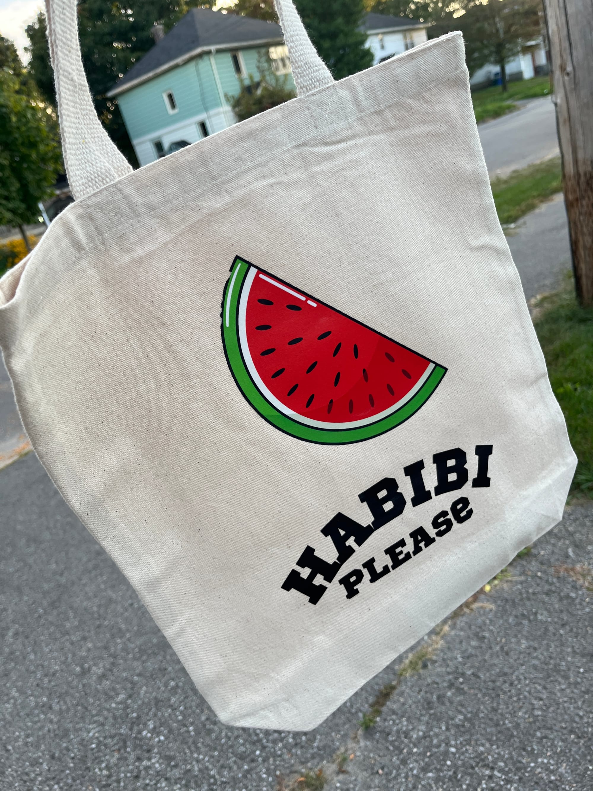 An off-white tote bag featuring a slice of watermelon and the words "Habibi Please" beneath it. 