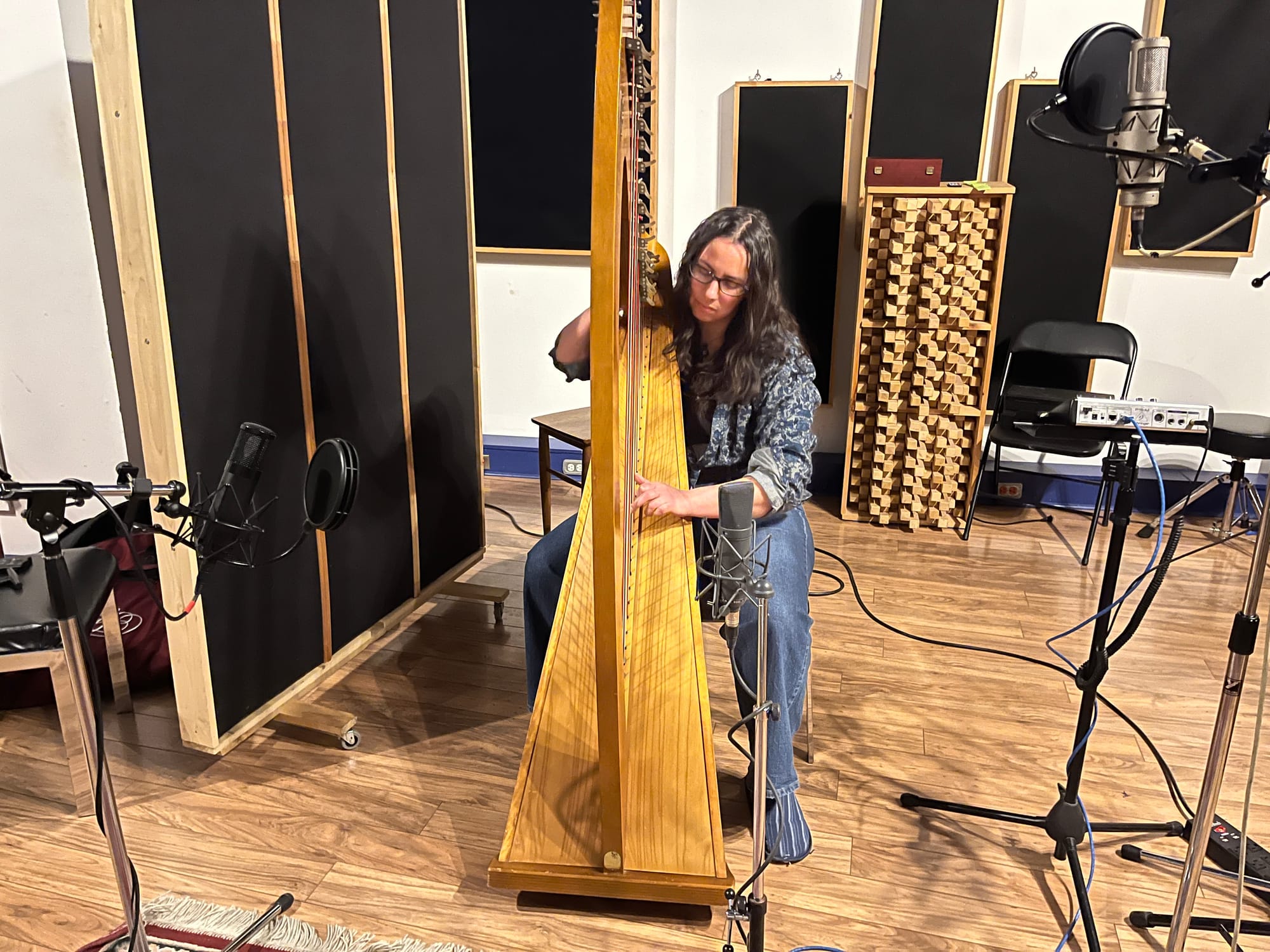 A photo of playing my 36-string Lyon & Healy Troubadour IV lever harp, in a recording studio, surrounding by microphones and author audio equipment.