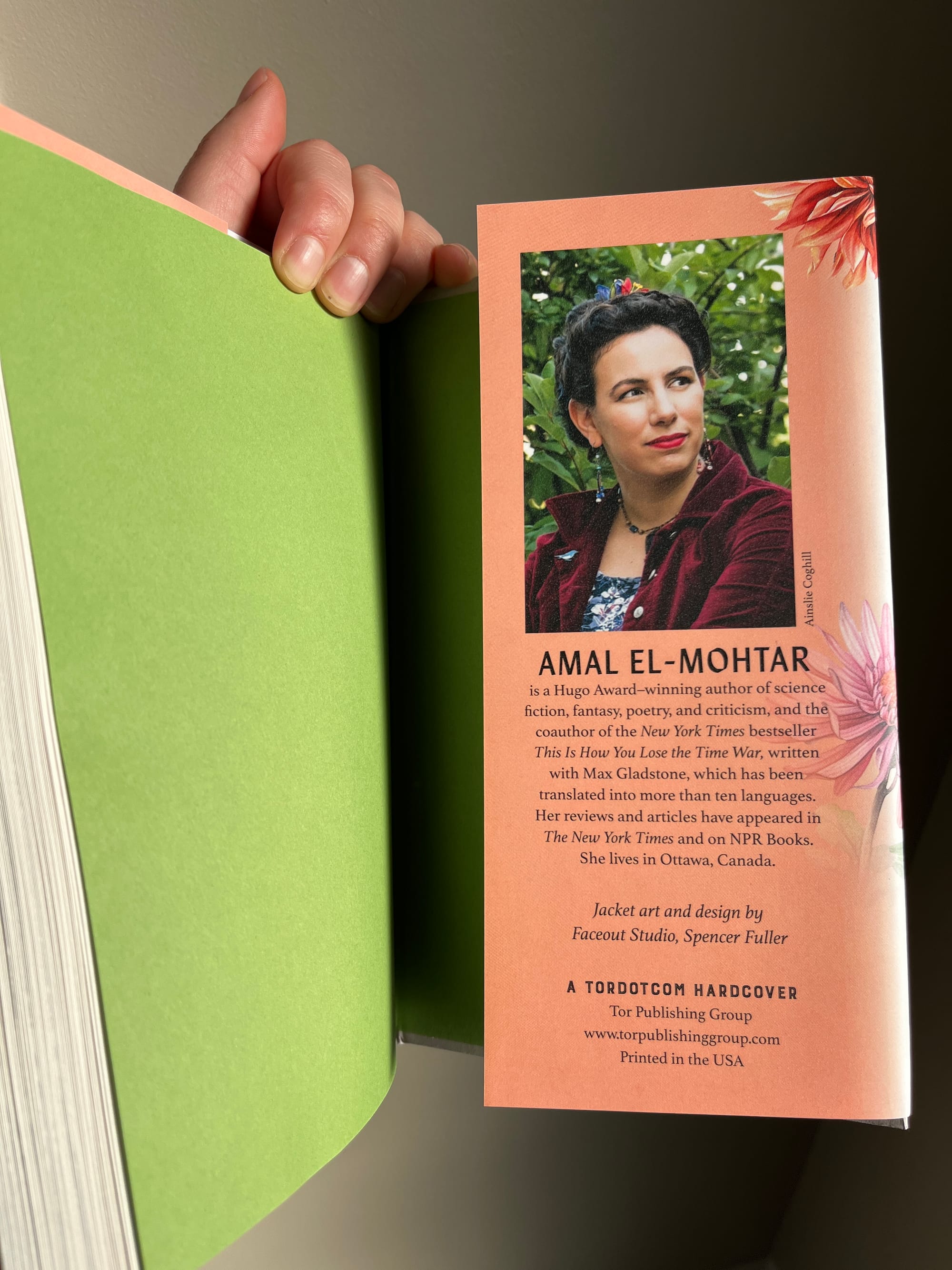 The back flap of the book, showing my author photo and bio, in which I'm wearing a red velvet red blazer over a dark blue floral dress and looking away from camera against a background of vibrant green leaves. The green of the end papers echoes the green of the leaves.