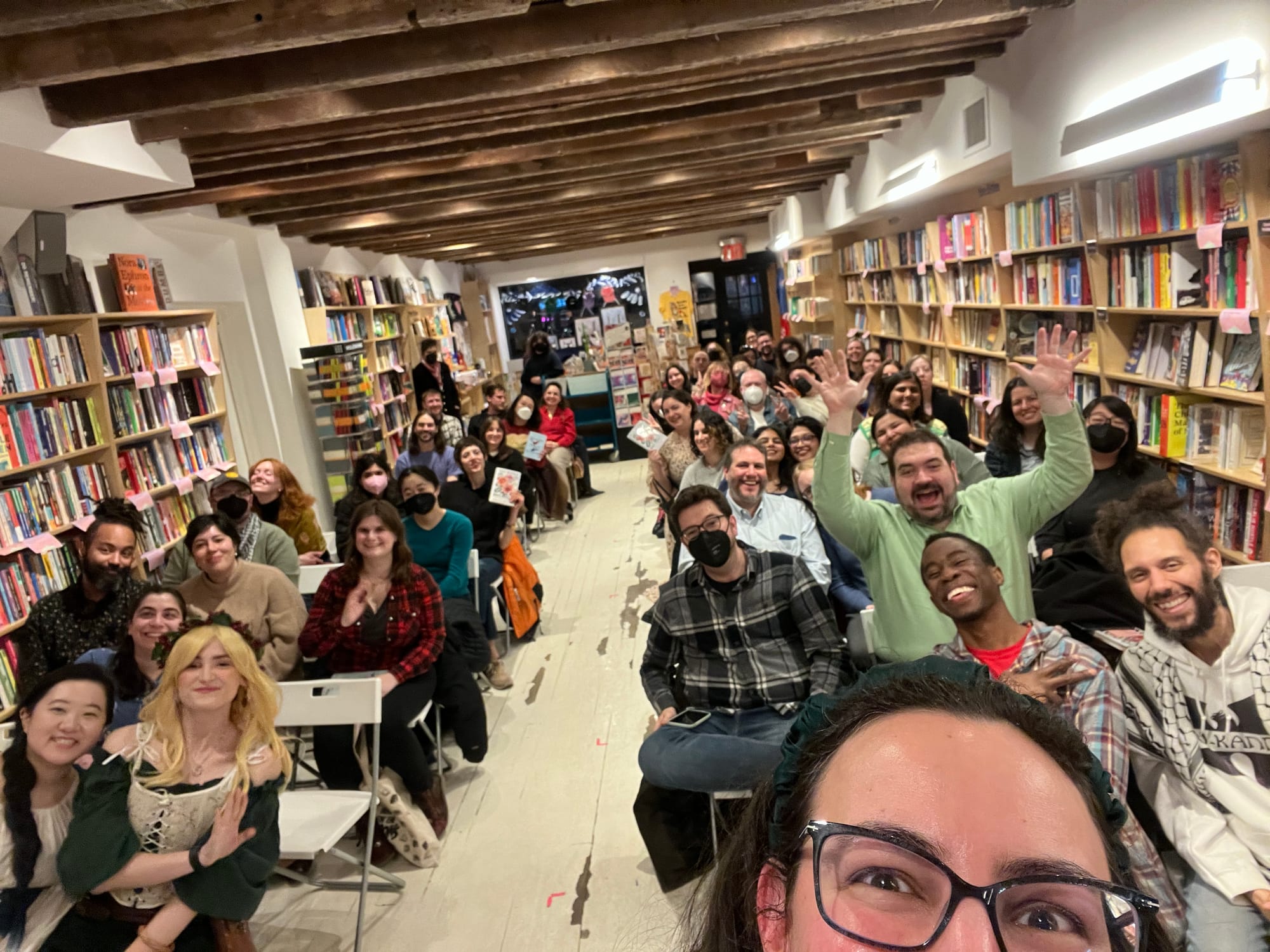 The top half of my face in the foreground as I attempt a bookstore selfie that encompasses the crowd of people assembled at Books Are Magic for my event with Helen Rosner. There are around 50 people in the room, organised into two sides with a central aisle; one man in the front row is lifting his arms in excitement.