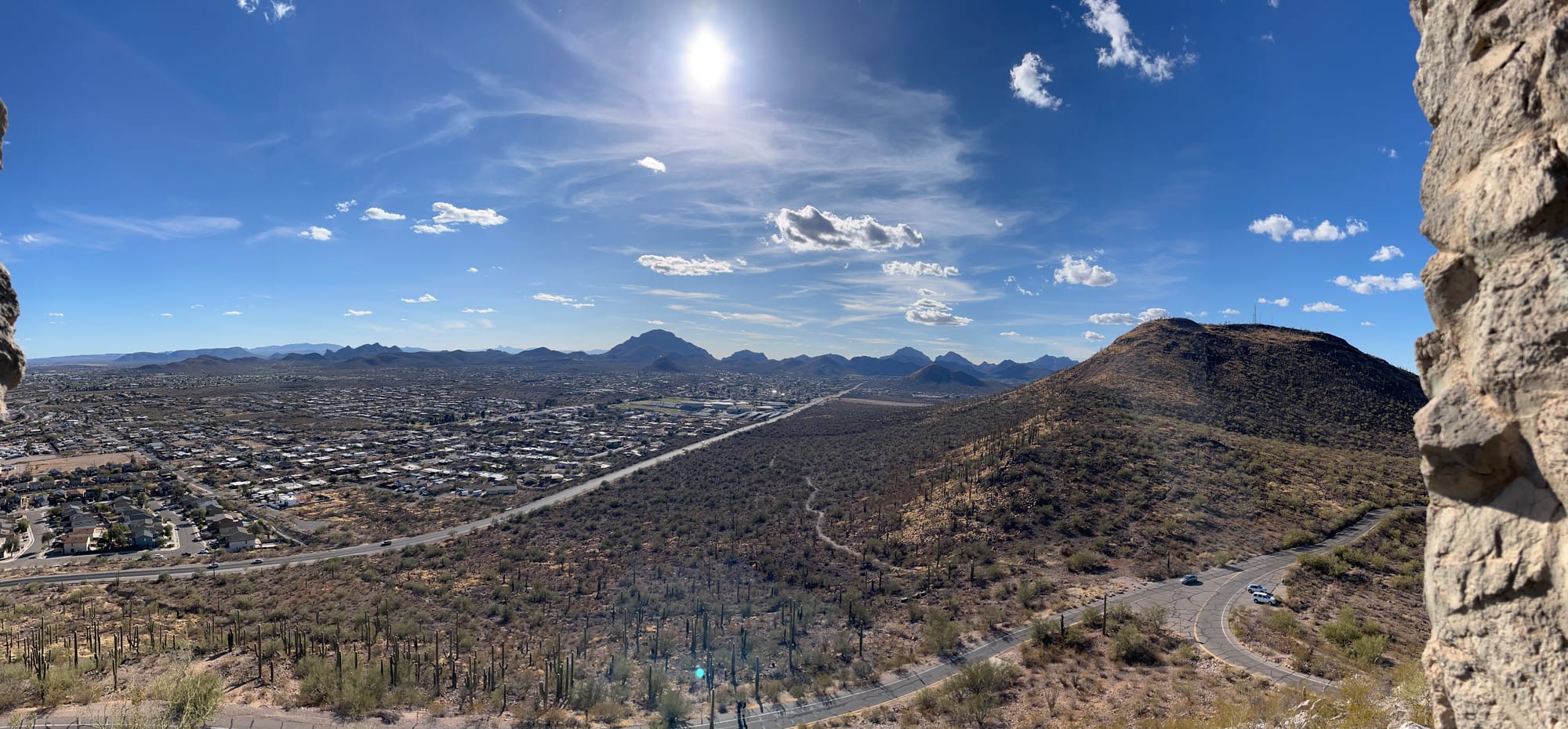 Under a wide blue sky dotted with white clouds, silhouetted mountains and a shining ribbon of road leading to them.