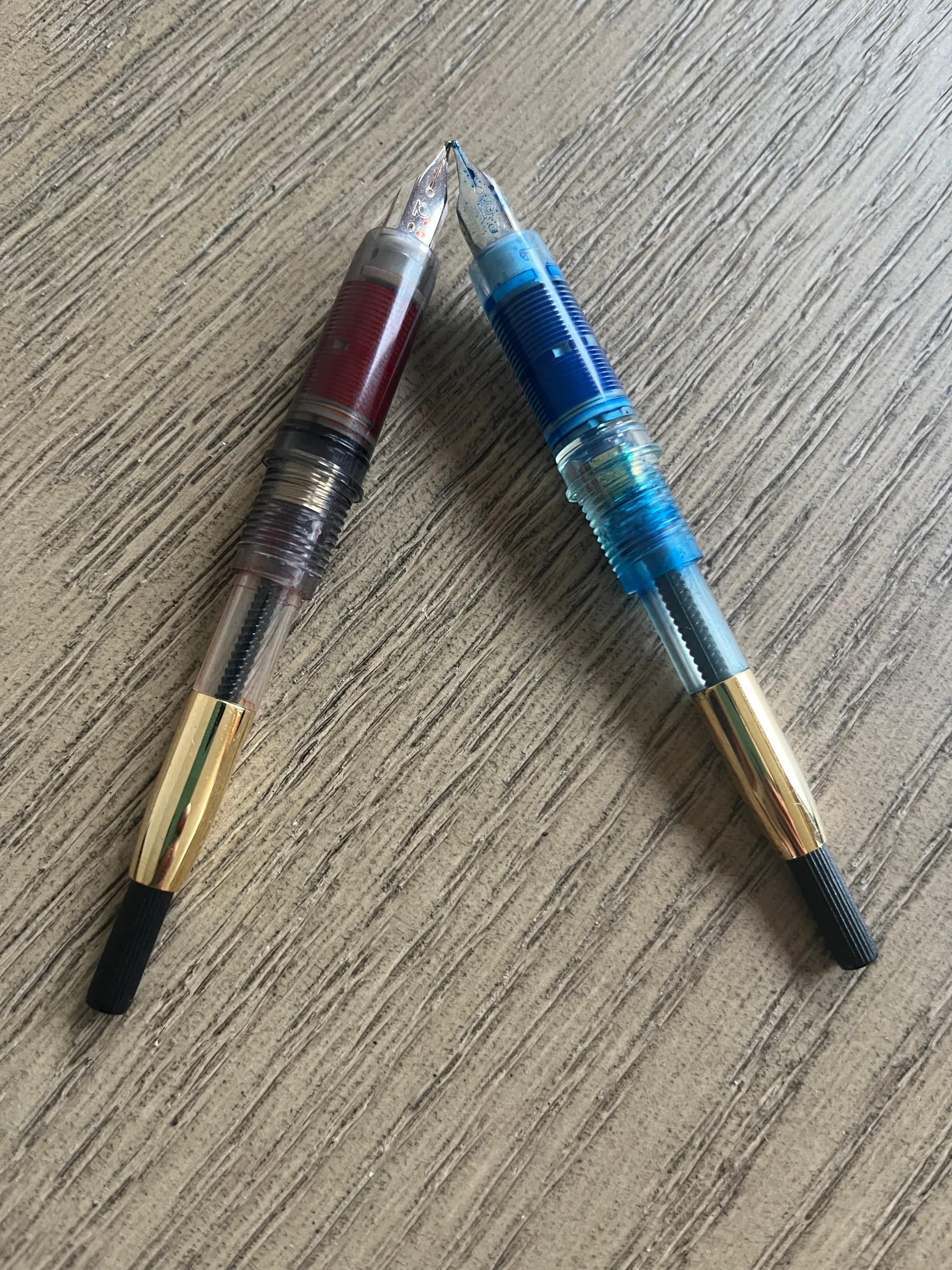 A pair of Platinum Plaisirs with their nibs angled towards each other, denuded to show their empty cartridges; one is stained by an orange ink called Yu-Yake, and the other by a blue ink called Kon-Peki.