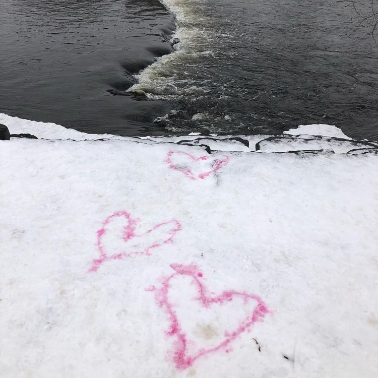 Foreground: snowy ridge abuts on to river in which a grey basketball is caught in a seam of rapids. 3 pink hearts lead to it.