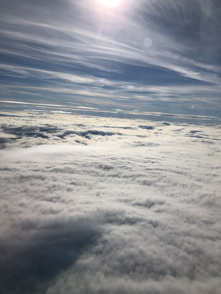 Cloudscape as seen from an airplane flying high above them: like if sand dunes were made of rushing white water.