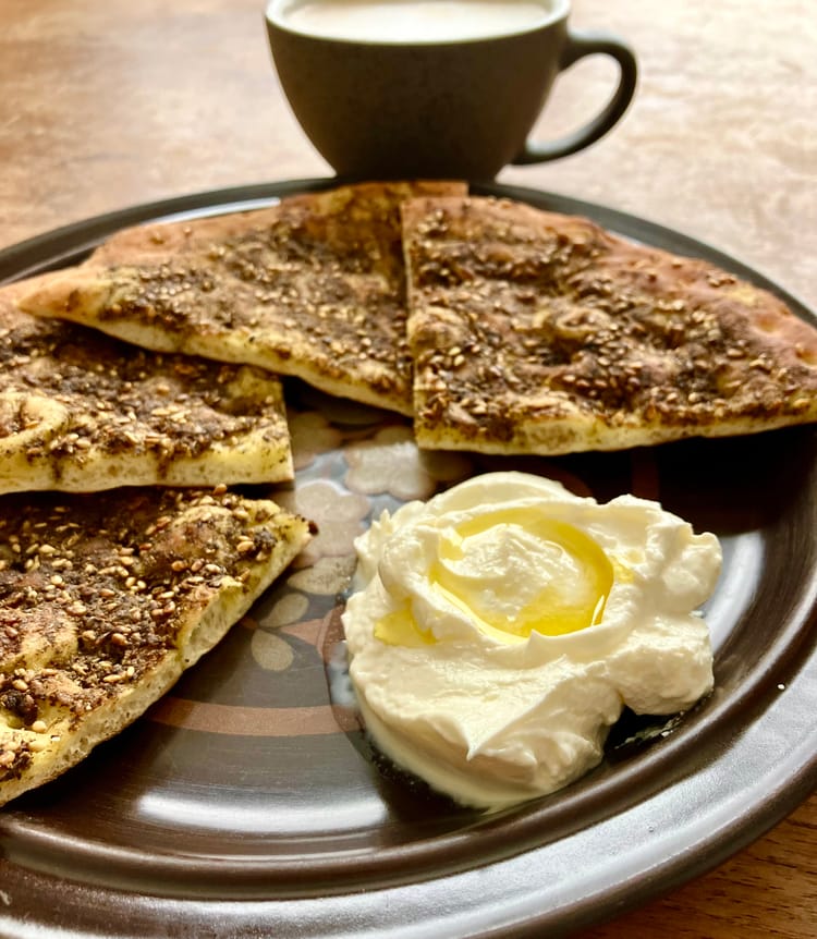 Close up on a dark brown plate holding a dollop of labaneh and triangles of zaatar flatbread called manaeesh.