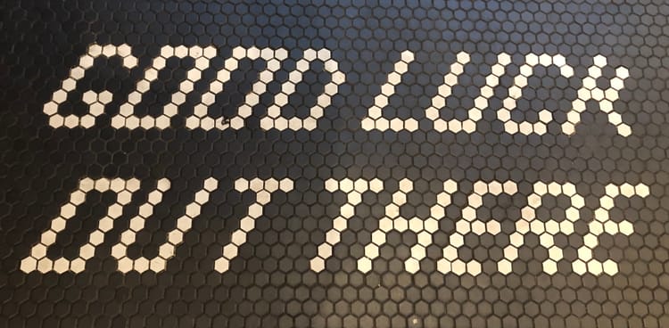 Photo of a honeycomb-tiled floor sign that reads "Good Luck Out There" in white on black.