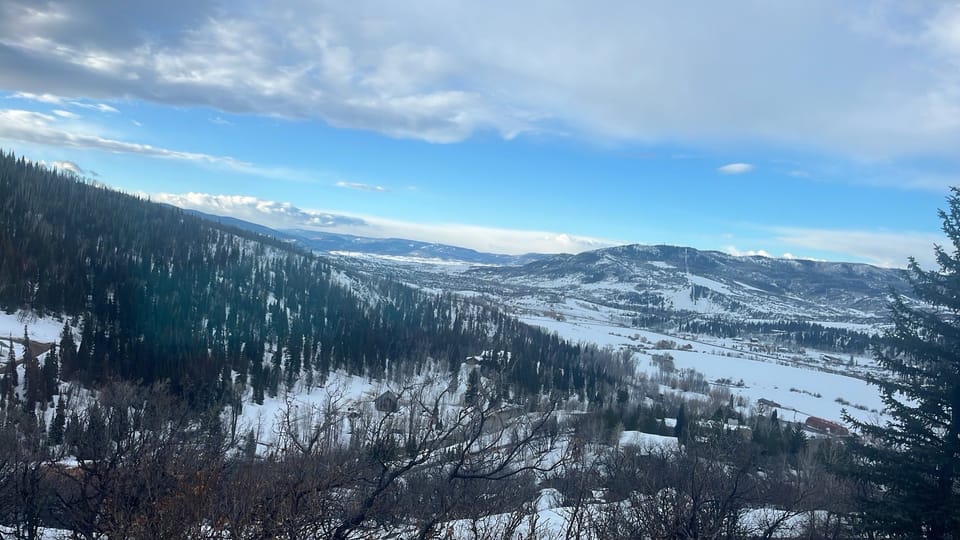 A snowy, pine-covered mountain range in Colorado, beneath a blue sky half-covered in white clouds.